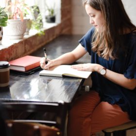 Woman sitting at table writing in a notebook.