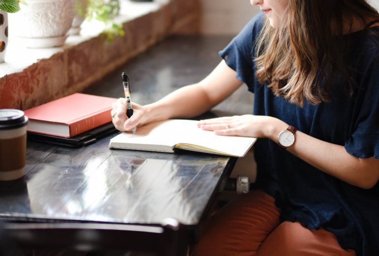 Woman sitting at table writing in a notebook.
