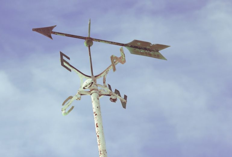 A weather vane with a partly cloudy sky in the background.