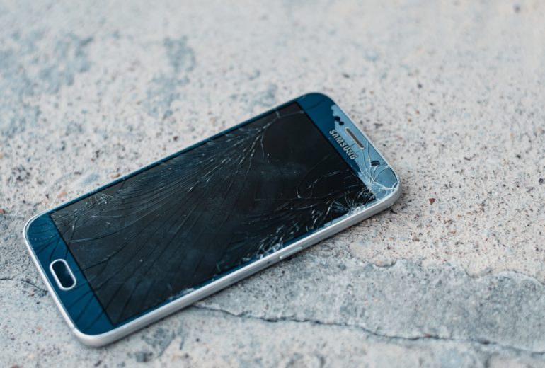 A cell phone with a shattered screen on a concrete floor.
