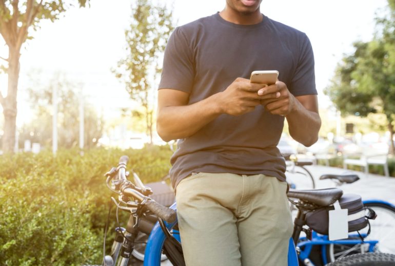 A man leaning on a bike texting on his phone.