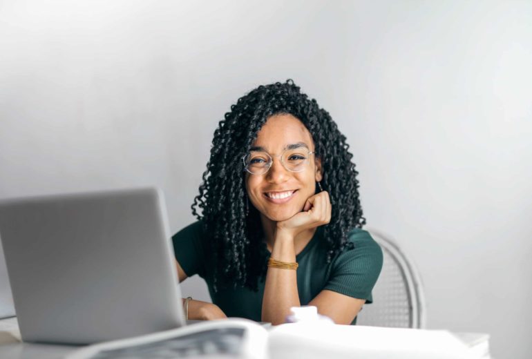 A smiling woman sitting at a table with a laptop.