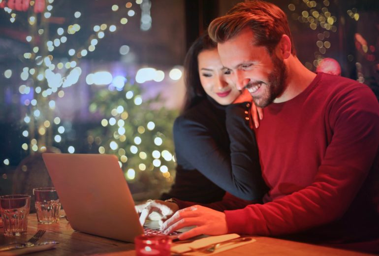 A smiling couple shopping on a laptop together.