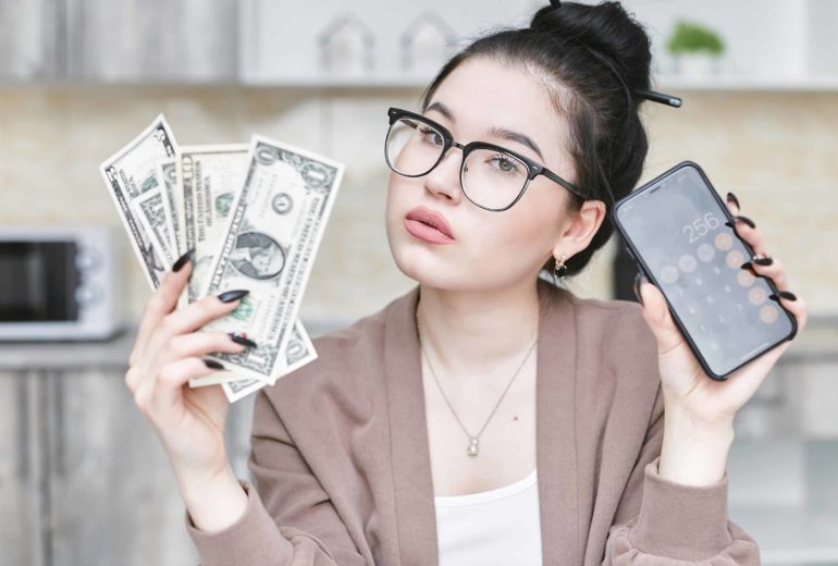 Woman with dollars in cash and using the calculator on her phone.