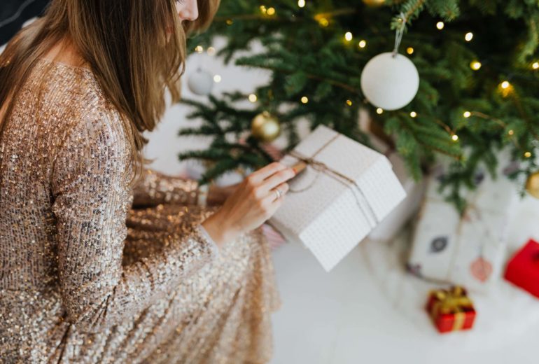 A woman looking at a Christmas present under a Christmas tree.