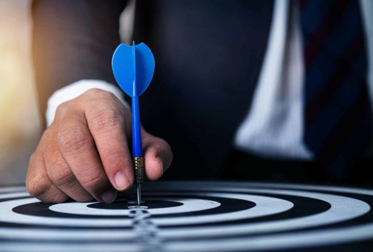 Conceptual photo of a man in a suit holding a dart to a dartboard.