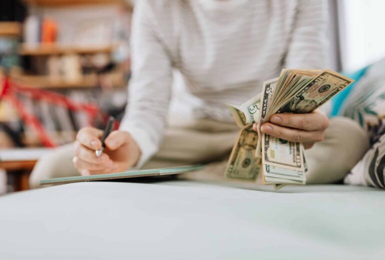 Person counting a stack of cash at a table, bills fanned in one hand with a blurred background.