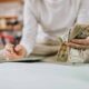Person counting a stack of cash at a table, bills fanned in one hand with a blurred background.