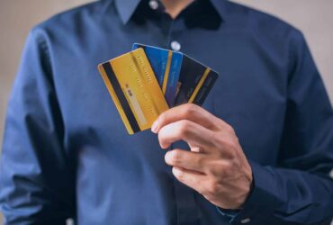 Person in a blue shirt fanning several colorful credit cards in hand, showing multiple cards at once.