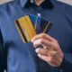 Person in a blue shirt fanning several colorful credit cards in hand, showing multiple cards at once.