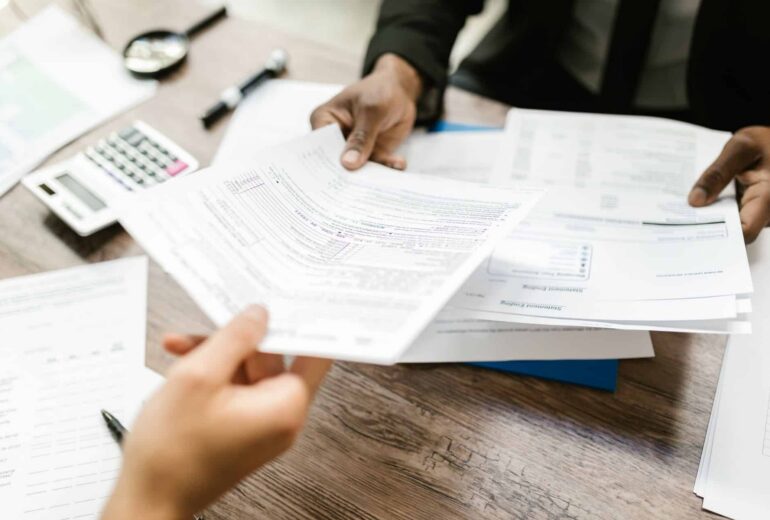 Hands sorting through financial documents on a wooden desk with a calculator nearby.