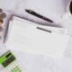 Desk scene with coins scattered beside envelopes, a black pen, a coffee cup, and a green calculator on a white marble surface.